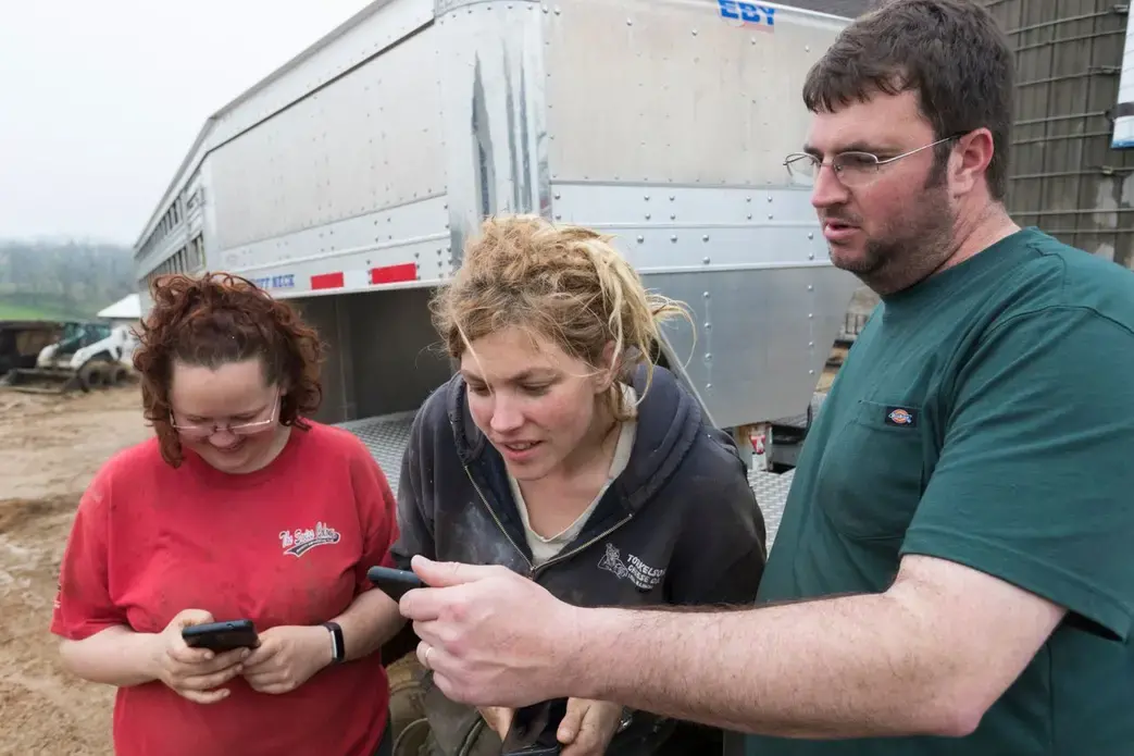 Truck driver and farmer Dan Richards, right, shares photos of his farm with Brandi, left, and Emily Harris. Image by Mark Hoffman. United States, 2019.