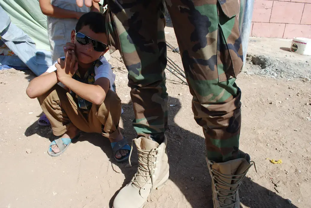 A young Syrian Kurd crouches in the shadow of Amin, a Syrian Kurdish soldier on break from training. Image by Jenna Krajeski. Iraq, 2012. Media file: DSC_1097.JPG