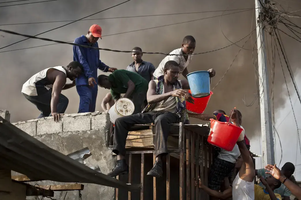 Residents of Camp Yaunde throw buckets of water on a quickly spreading fire, as firefighters stood helpless because their water tanks were empty. Image by William Sands, Equatorial Guinea, 2011. Media file: Equatorial-Guinea-Will-Sands.jpg