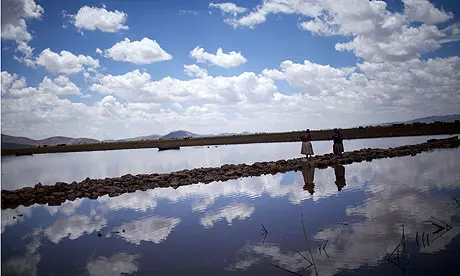Aymara women cross a bridge of rocks on the shores of Lake Titicaca. The lake's water is increasingly contaminated by rivers that pass through the industrial city of El Alto. Image by Noah Friedman-Rudovsky. Bolivia, 2011. Media file: Lake-Titicaca--Aymara-wom-007.jpg