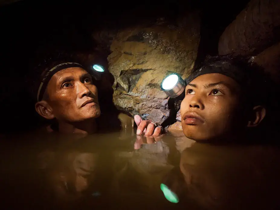 An older miner and a younger boy are chin deep in frigid water 150-meters below the surface as they work a gold mine near Syndicate on the island of Masbate. Image by Larry C. Price. Philippines, 2012. Media file: Price Photo Week Slide Show004.jpg