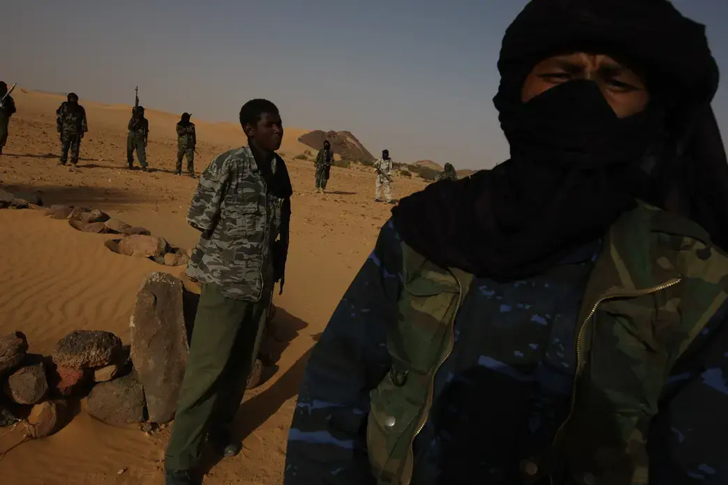 A Niger army soldier, taken prisoner by Tuareg rebels, stands in front of the grave of a civilian he is accused of murdering in the Aïr Mountains. The deceased was the father of the Tuareg commander (foreground), who would later decide the prisoner's fate. Image by Brent Stirton. Niger, 2011. image