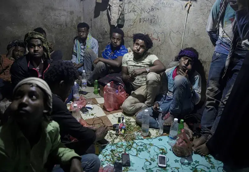 Ethiopian migrants chew qat, as they take shelter, Aug. 4, 2019, in a small shack at a qat market in Dhale province, one of the stops where migrants take shelter to continue their journey to Saudi Arabia, and an active frontline between Houthi rebels and militiamen backed by the Saudi-led coalition. Imageby AP Photo / Nariman El-Mofty. Yemen, 2019.