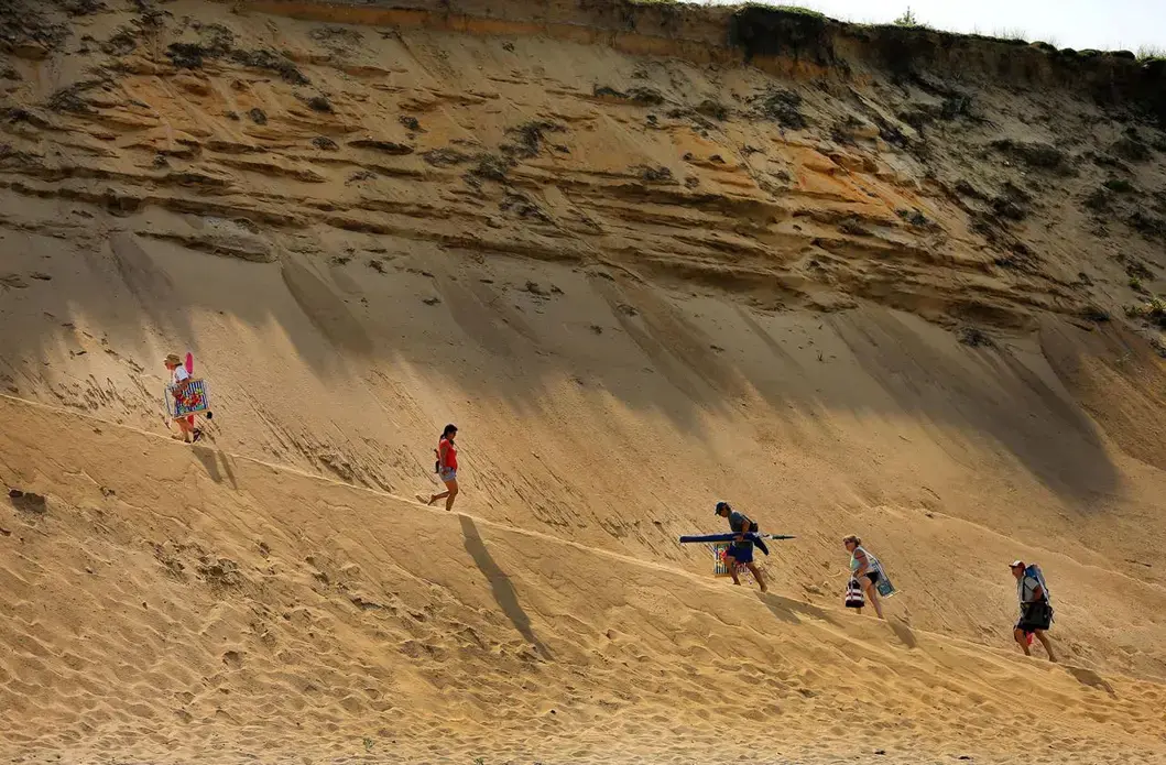 Beachgoers made the steep climb up a towering sand dune cliff from White Crest Beach to the parking lot above. Image by John Tlumacki. United States, 2019.