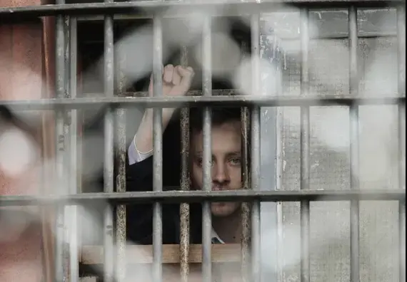 A Belarussian detainee, arrested during the flash mob in Minsk on July 7, gestures from a prison cell at a detention centre. Image by Vasily Fedosenko, Reuters. Minsk, Belarus, 2011. image