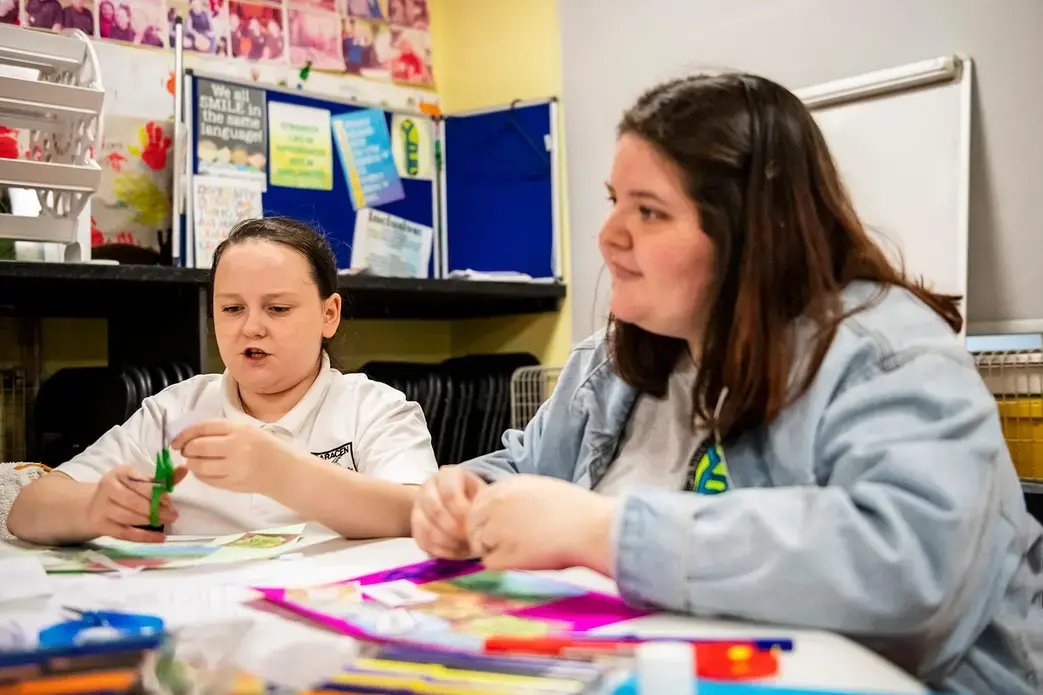 Chloe Crichton, 11, left, cuts out pictures for a vision board during an arts and craft session led by Kelsey Reilly, 19, a Young People's Futures apprentice. Image by Michael Santiago. United Kingdom, 2019.