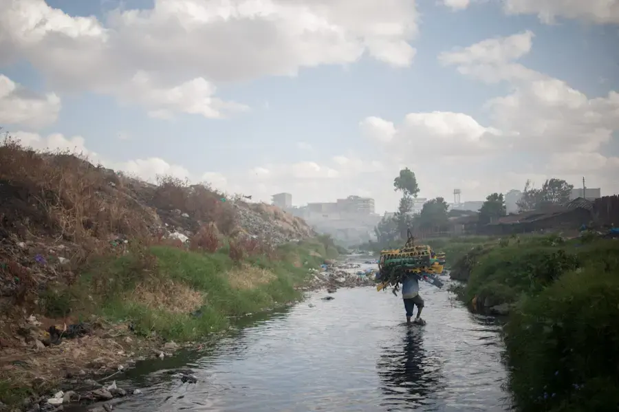Man walking through the water of the Nairobi River, carrying scavenged rubber material in hopes of selling it to recycle facilities. Image by Micah Albert. Kenya, 2012. Media file: dandora-kenya-micahalbert.jpg