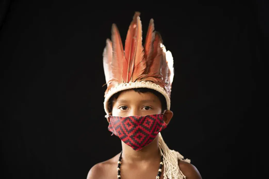 Six-year-old Elano de Souza, of the Sateré Mawé indigenous ethnic group, poses for a portrait wearing the traditional dress of his tribe and a face mask amid the spread of the new coronavirus in the Gaviao community near Manaus, Brazil, Friday, May 29, 2020. Image by Felipe Dana / AP Photo. Brazil, 2020.