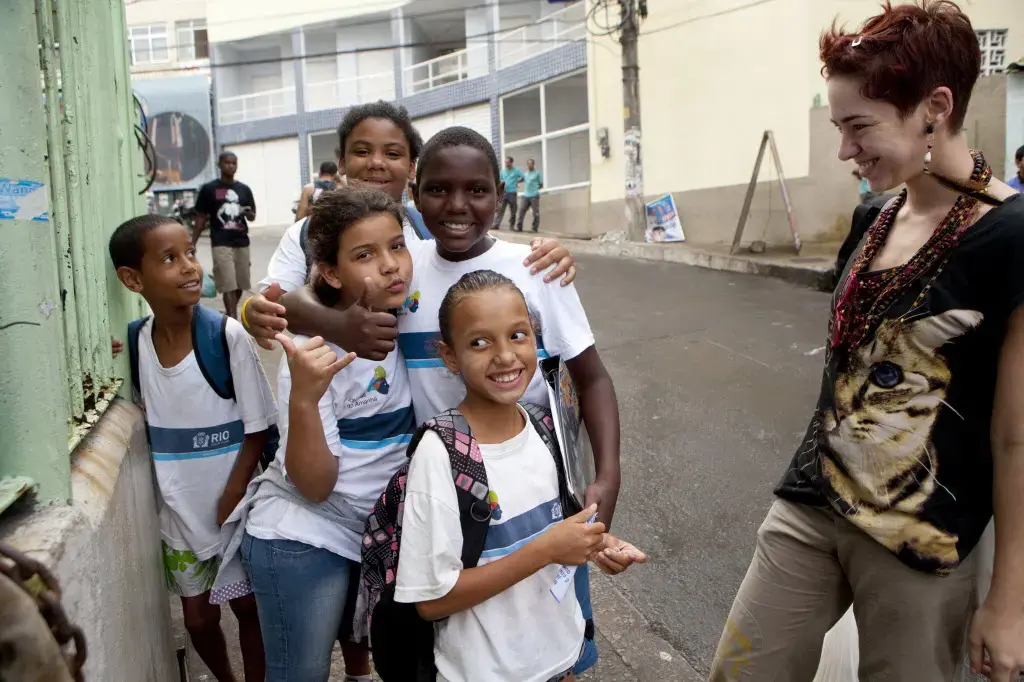 Tatiana Coelho chats with schoolchildren in the Rio de Janeiro favela she now calls home. Coelho, who is Portuguese, came to Brazil a year ago because of all the job opportunities - and because of the weak economy back home. She is an artist. She says she enjoys living in the favela because there is more humanity here, that it is real life. Image by Melanie Stetson Freeman. Brazil, 2012 Media file: favela_tatiana.jpg