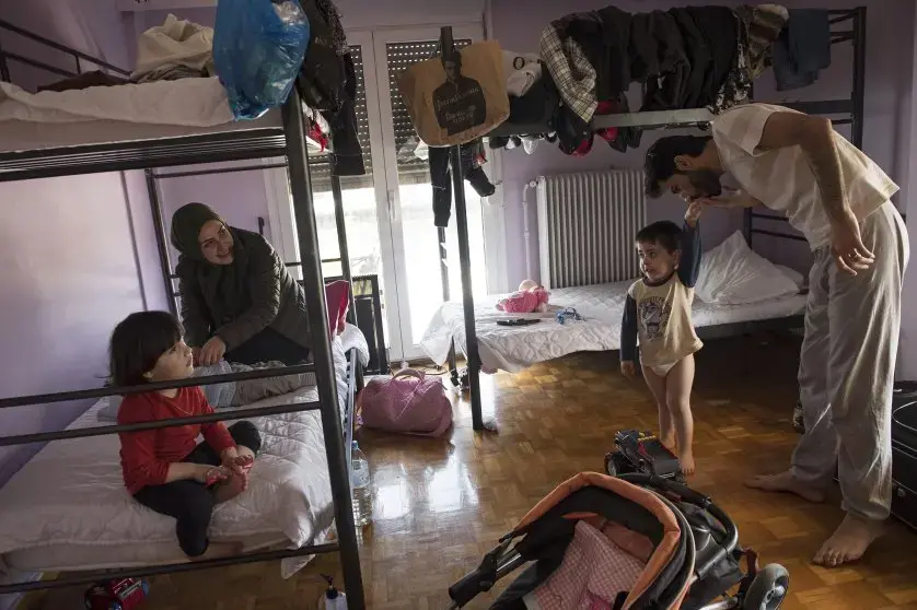 Syrian refugee, Taima, prepares to take her 6-month-old daughter, Heln, for a visit to the Acropolis, while her husband, Muhannad Abzali, 28, jokes around with their other child, Wael, 3, at the temporary apartment they are staying at in Athens. Image by Lynsey Addario. Greece, 2017.