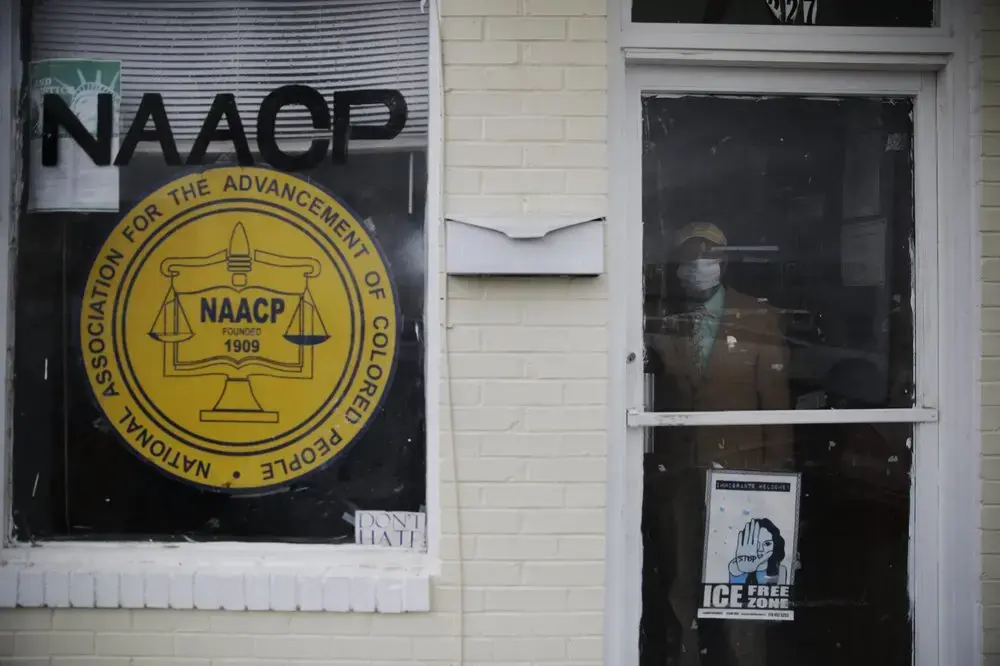The Rev. Ezekiel Holley, 78, of Dawson, Ga., a leader of the NAACP, looks out from behind the office door window wearing a protective mask on Sunday, April 19, 2020, amid the COVID-19 coronavirus outbreak in Dawson, Ga. Image by Brynn Anderson / AP Photo. United States, 2020.