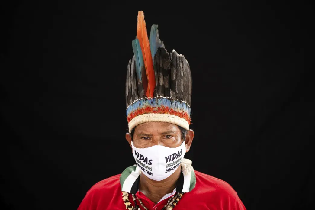 Indigenous leader Jose Augusto, 48, of the Miranha indigenous ethnic group, poses for a portrait wearing the traditional dress of his tribe and a face mask amid the spread of the new coronavirus at the Park of Indigenous Nations community in Manaus, Brazil, Thursday, May 28, 2020. Image by Felipe Dana / AP Photo. Brazil, 2020.