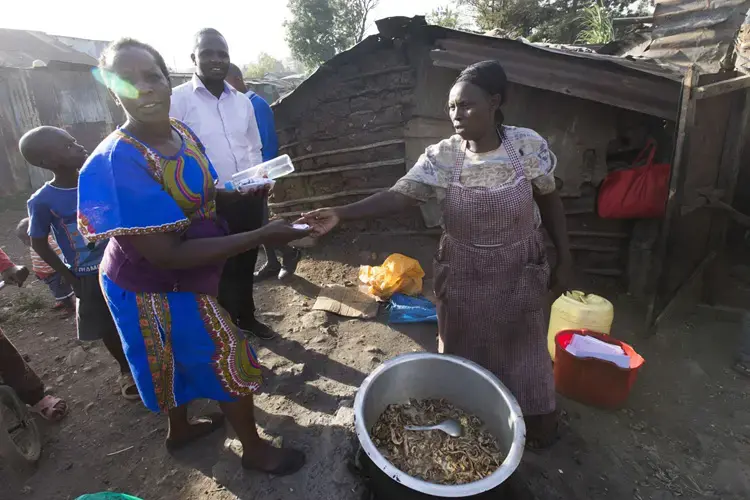 A woman sells a small mixture of chicken intestines and innards and immature eggs wrapped in sheets of used office paper for about 10 cents outside her home in the Korogocho slum. She has been making and selling the mixture for 30 years and was able to help pay for a son to attend a university. Image by Mark Hoffman. Kenya, 2017.