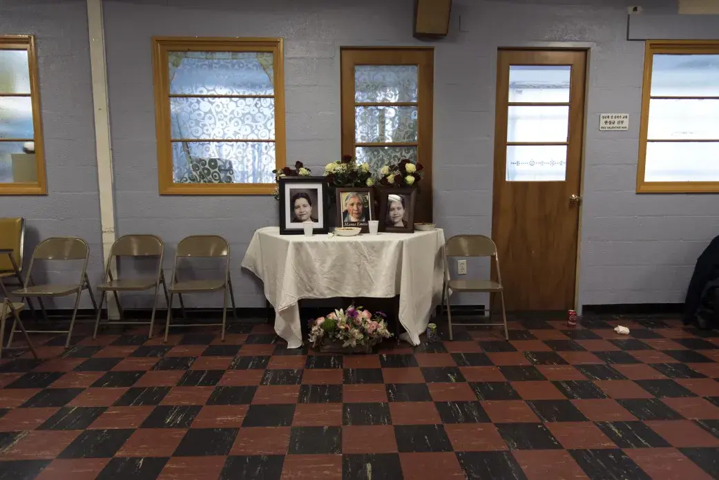 Photos displayed in the basement of a church attended by Emma Cespedes who died April 2, 2016 in Tarata, Bolivia. Her children, grandchildren, and surviving brother live in Virginia. She requested that all Bolivian traditions be followed, including her burial and subsequent masses following nine days of burial, one month of burial, six months of burial, and one year of burial. Her seven children and most of her grandchildren traveled to Tarata for her wake and burial. Her grandchildren returned to organize the ninth day mass for the Tarateño community in Virginia, which took place on the same day, and at the same hour as the ninth day mass being held by their parents in Tarata. “She was a mother for everyone, not just for our family. Her heart was so big… I know that many of you feel an immense sadness. Our family is celebrating at this same hour in Bolivia. It’s very difficult to express, but thank you for accompanying us,” said Faviola, one of Emma’s grandchildren, speaking at the end of the Virginia mass. Image by Carey Averbook. United States, 2016.
