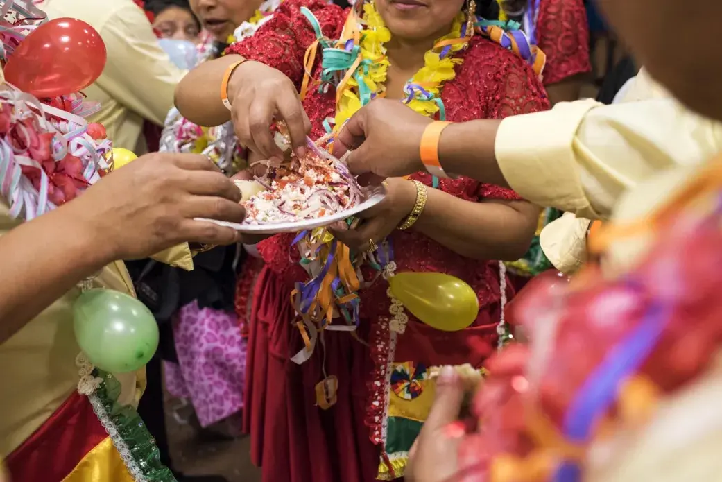 A group of friends share a traditional q’allu salad of tomato, onion, and cheese. These friends are part of a music and dance group, which are called comparsas, and they go by “Los Renegados” or “The Renegades.” At every carnival party, each comparsa presents their prepared dance and perform Quechua/Spanish couplets for the couplet competition. People in each group match their clothing and celebrate the night together. Image by Carey Averbook. United States, 2016.
