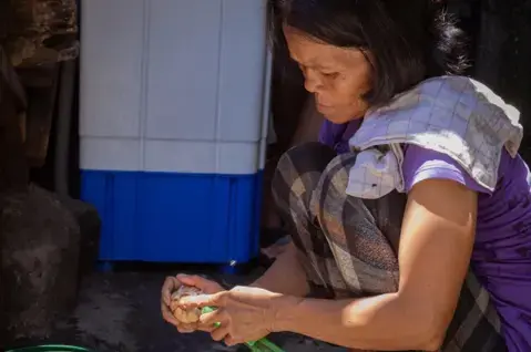 Rosemary Herela, 41, makes a living from peeling two sacks of garlic every day. Image by Micah Castelo. Philippines, 2019.