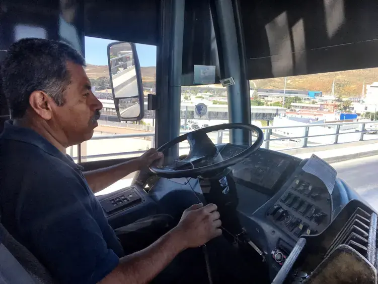 Margarito Cruz Gallarno steers his bus past the San Ysidro Port of Entry. Image by Patrick Reilly. Mexico, 2017.<br />

