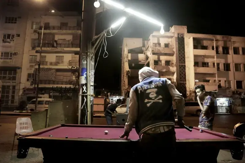In this Feb. 15, 2018, photo, youth play pool on a street in front of damaged buildings due to the war in Aden, Yemen. Many damaged buildings are hollowed-out versions of their former selves, a testament to lives and hopes once lived by inhabitants who now scrape by on aid handouts and the bare minimum for survival. Image by Nariman El-Mofty. Yemen, 2018. </p>
<p>