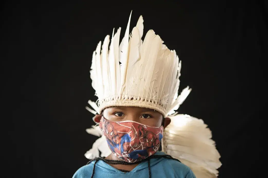 Six-year-old Ezinaldo dos Santos, of the Sateré Mawé indigenous ethnic group, poses for a portrait wearing the traditional dress of his tribe and a face mask amid the spread of the new coronavirus in the Gaviao community near Manaus, Brazil, Friday, May 29, 2020. Image by Felipe Dana / AP Photo. Brazil, 2020.