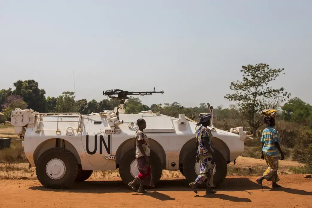 Women walk past a U.N. vehicle at the entrance to the sprawling camp in Kaga-Bandoro for thousands of families displaced by civil conflict. Image by Jack Losh. Central African Republic, 2018.