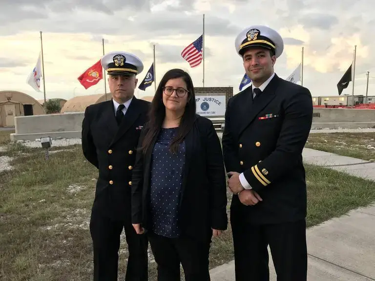 Pentagon paid attorney Susan Hensler, center, is the lead defense counsel for the former CIA captive charged as Abd al Hadi al Iraqi. At left is Navy Lieutenant Charles D. Ball III and at right is Navy Lieutenant Dahoud A. Askar, both detailed defense attorneys in the al-Qaida commander case. They pose at the Camp Justice sign at the U.S. Navy base at Guantánamo Bay, Cuba, in this image approved for release by a U.S. military officer. Image courtesy of Carol Rosenberg.