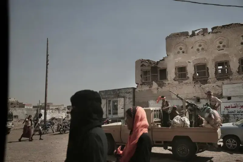 In this Feb. 12, 2018, photo, women walk past Saudi-led coalition backed forces, who are leading the campaign to take over Hodeida, as they patrol Mocha, a port city on the Red Sea coast of Yemen. Violence, famine and disease have ravished the country of some 28 million, which was already the Arab world’s poorest before the conflict began. The conflict pits a U.S.-backed, Saudi-led coalition supporting the internationally recognized government, which has nominally relocated to Aden but largely lives in exile, against rebels known as Houthis. Image by Nariman El-Mofty. Yemen, 2018. </p>
<p>