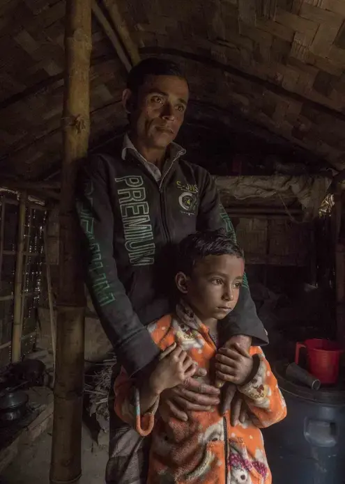 Workers like Mohammad Esarul Molla, 28, and his daughter Moumita, age 6, reside in huts on the factory property. While the air is often hard to breathe, the job is welcomed. Image by Larry C. Price. Bangladesh, 2018.