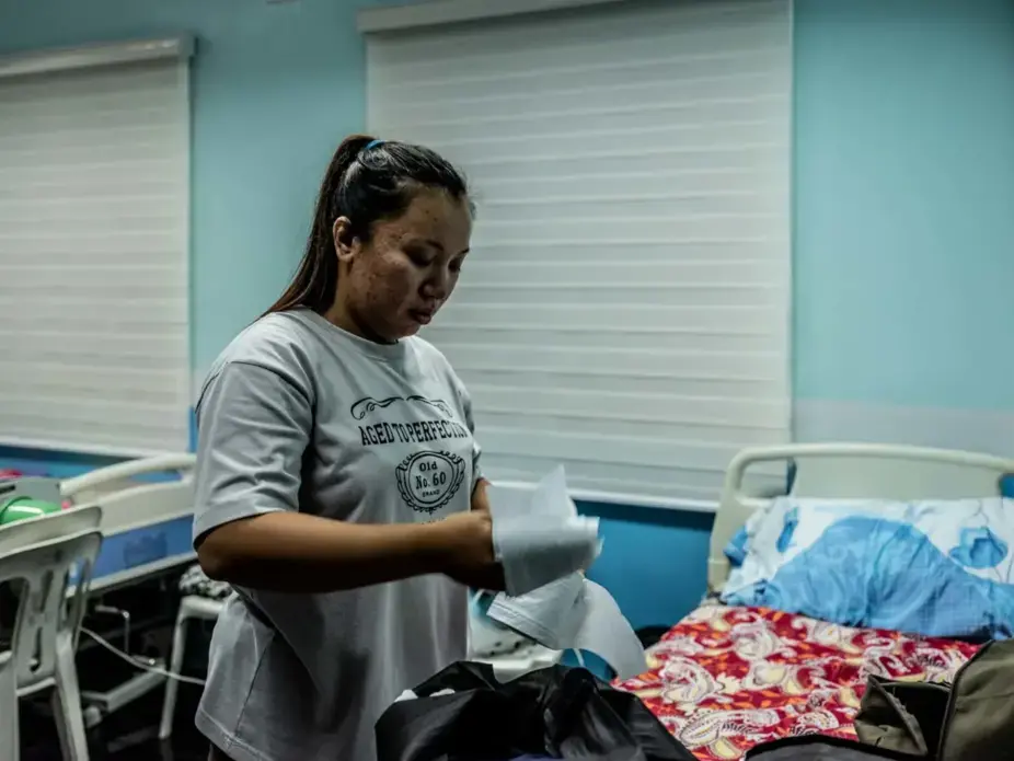 Lady Eleponga, a midwife working under a 3-month contract who is now working to prevent the spread of the virus, prepares her cloth mask by using tissue paper as an added protection. Image by Xyza Bacani. Philippines, 2020.
