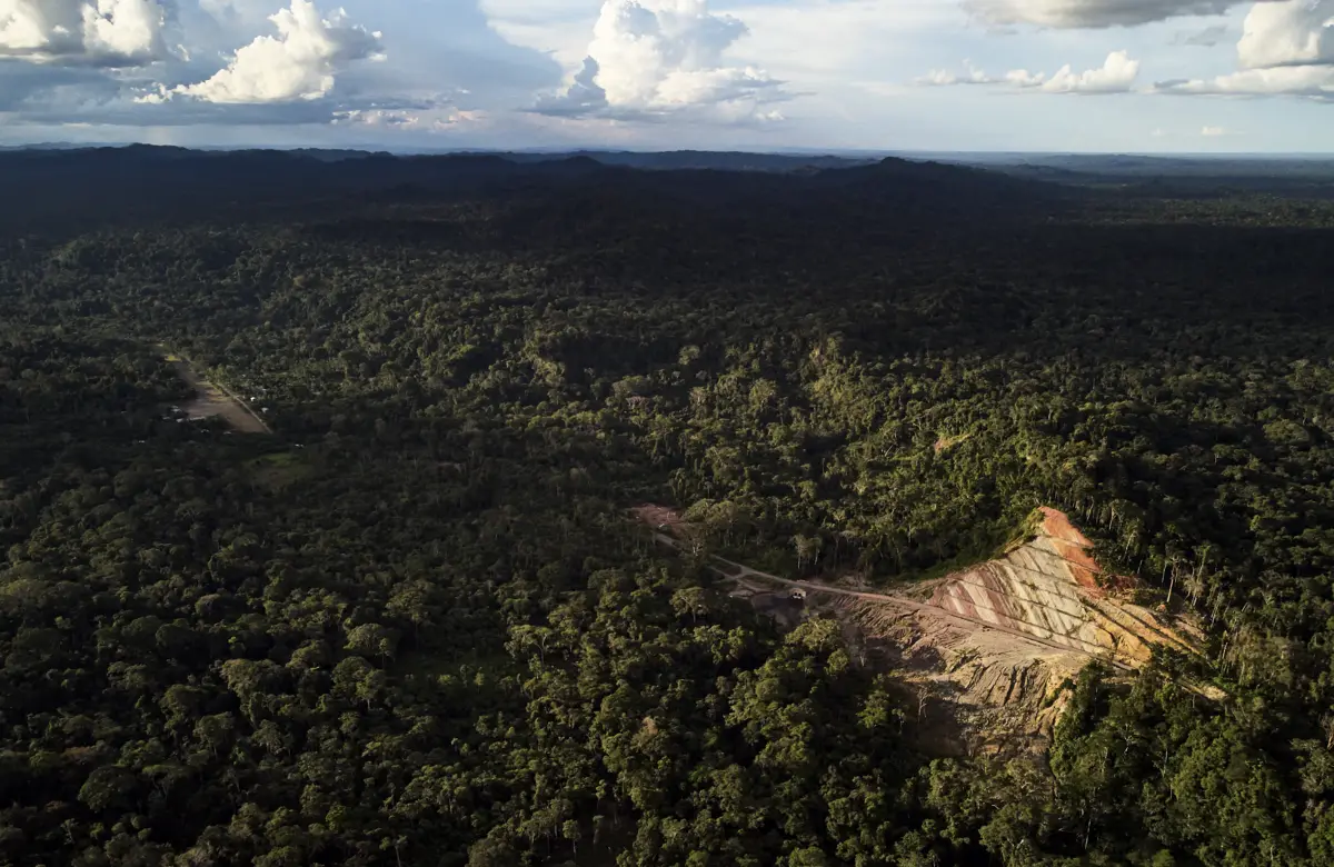 Aerial image of a road breaking through the Amazon Rainforest. The sky is blue and filled with clouds. 
