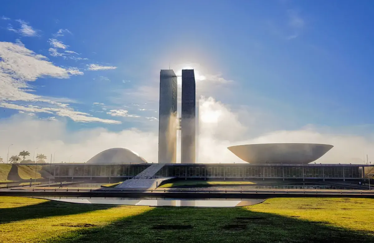 There is grass and a water fountain. Two skyscrapers are in the foreground. 