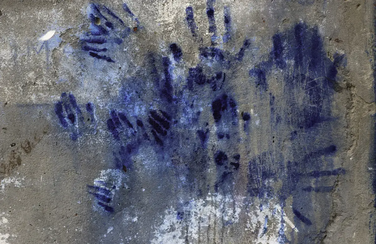 A close-up shot of layers of inky blue handprints covering a concrete wall