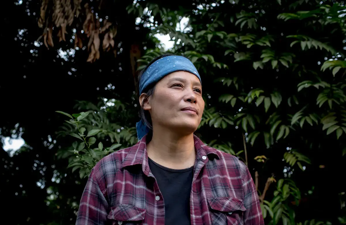 a woman wearing a blue headband smiles serenely against foliage