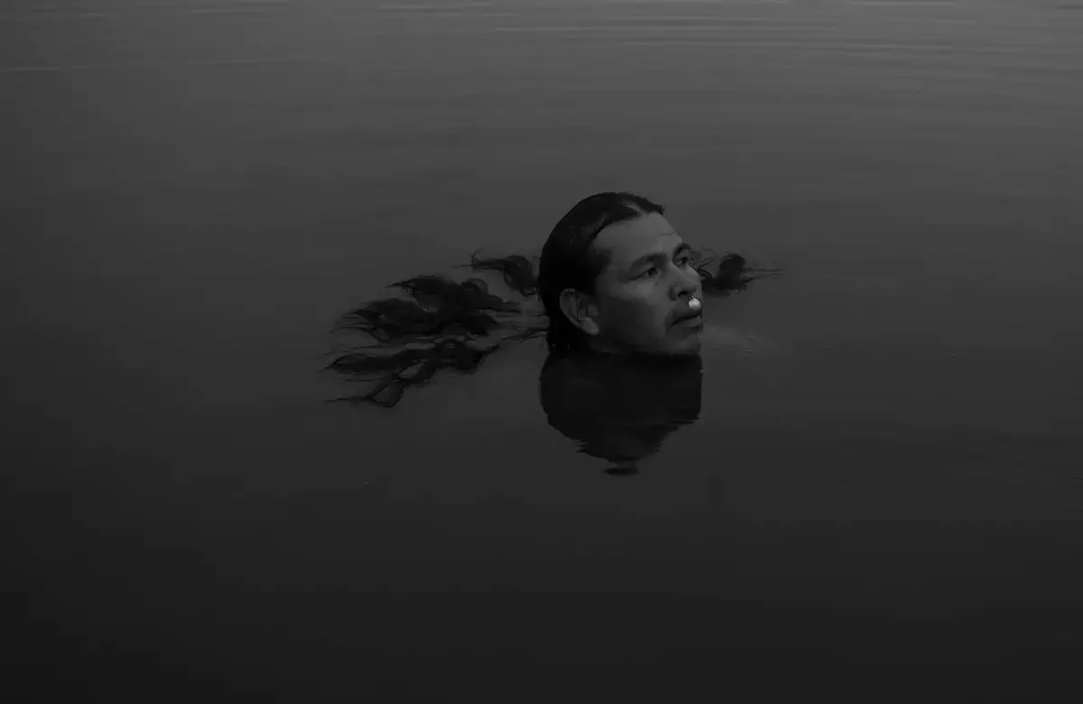 a man floats in a dark pool of water with his hair floating out behind him