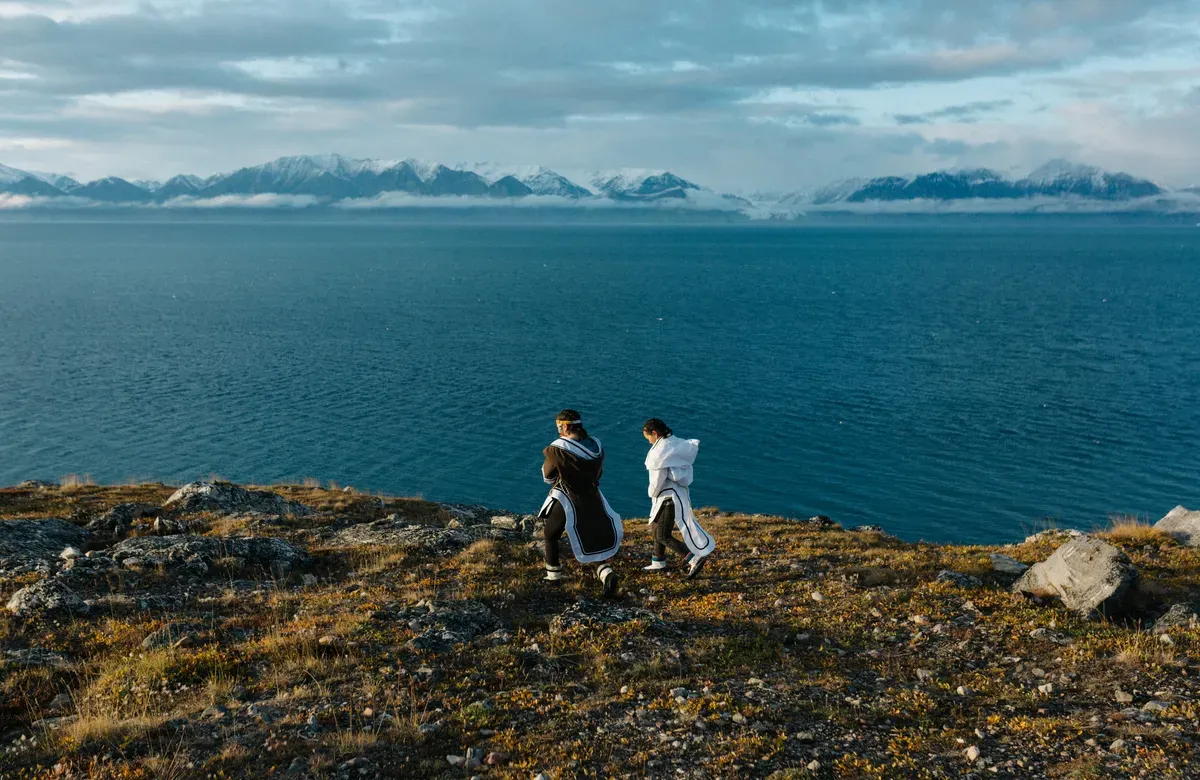 Two people walk near a cliff overlooking the water in the Canadian Arctic.