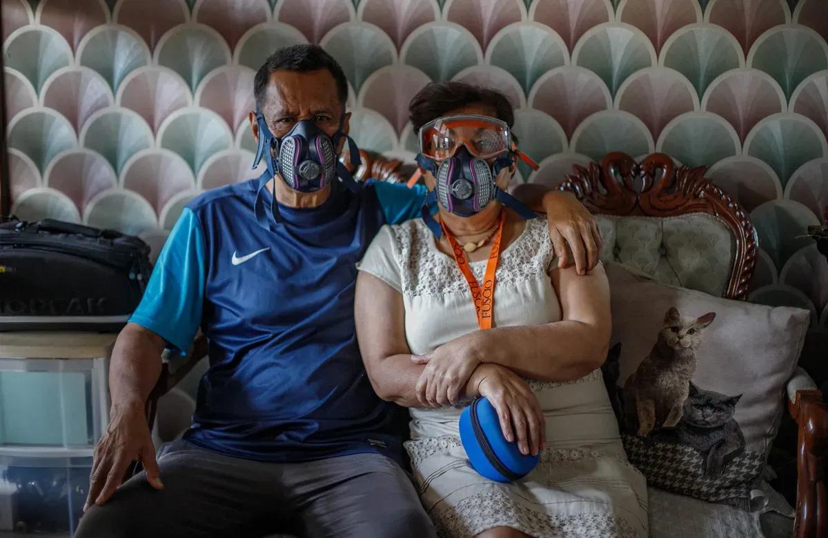 two people sit on a couch posing for the camera wearing a full face mask and goggles