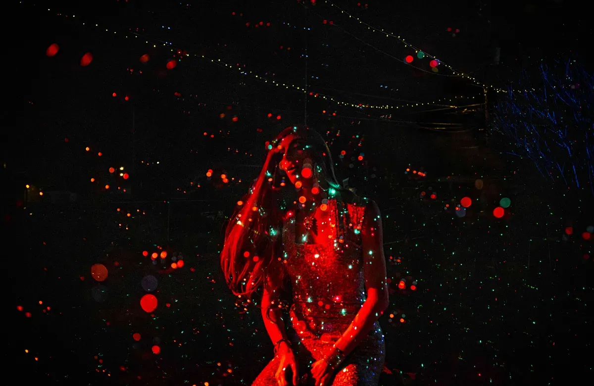 A drag queen stands out in the dark and disco lights lit up in red