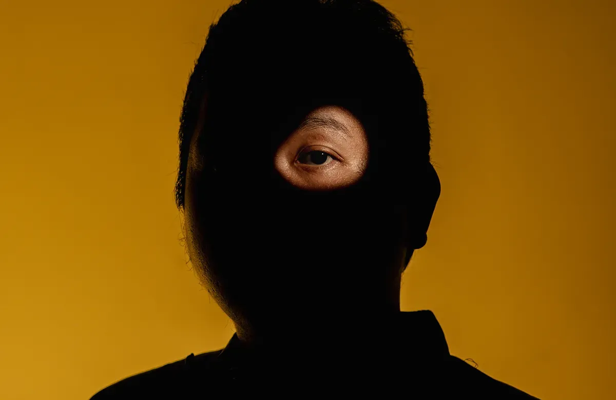 a person shrouded in shadow except for a circular light over one eye