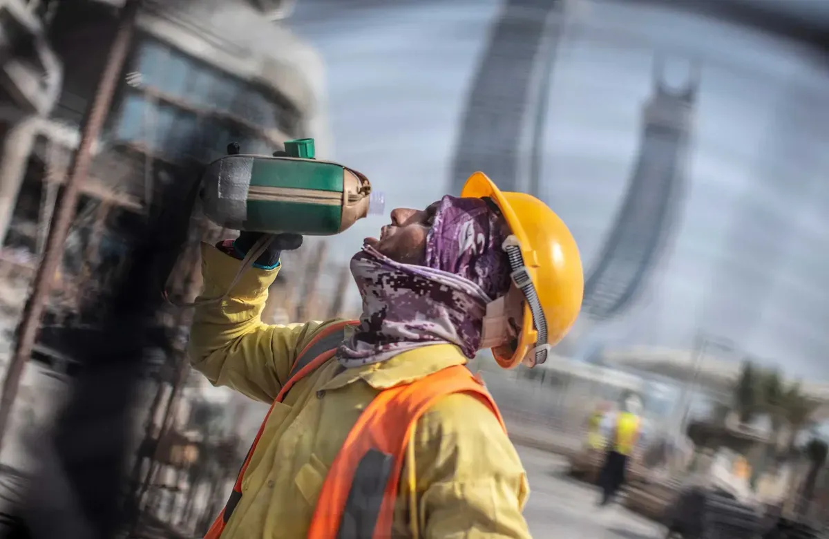 a worker wearing construction gear throws their head back to drink from a water bottle