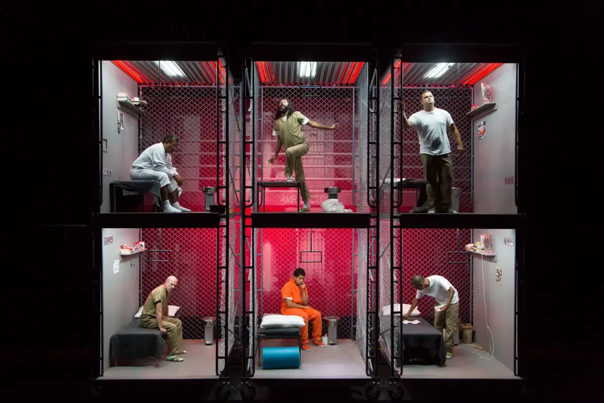 Image of actors in multi-level prison cells on a stage during a performance of The BOX.