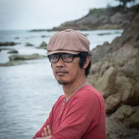 TaufikWijaya.jpeg A person wears glasses, a brown baseball cap, and a red shirt.