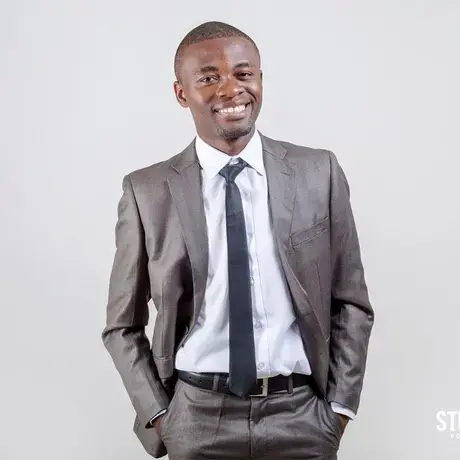 A person wearing a grey jacket, white shirt, and black tie smiles at the camera.