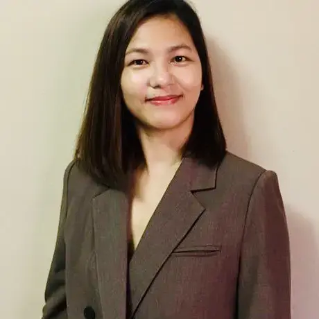 A person wears a brown jacket and has shoulder length black hair.