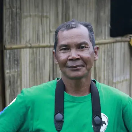 A person wears a green shirt and a camera strap.