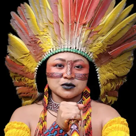 A woman with red makeup, yellow shirt and indigenous headress stares at the camera