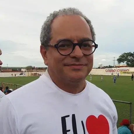 A man with grey curly hair and glasses stares into the camera