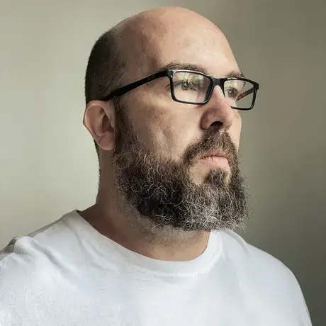 Man with a beard and black glasses looks to the left