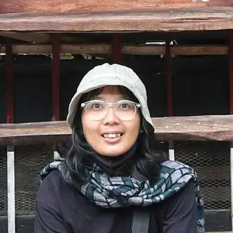 A person wears a cap and glasses. She is also wearing a black long sleeve shirt.