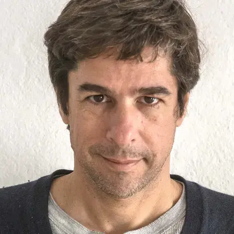 A man with short brown hair, a black sweater and grey shirt.