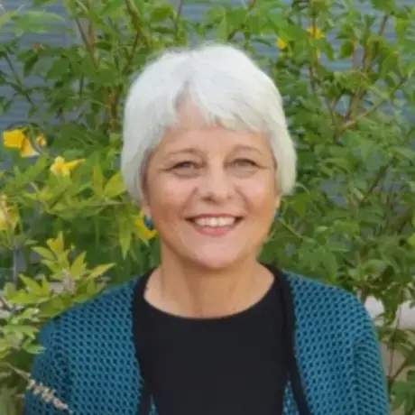 A woman with short gray hair wears a black shirt and blue sweater