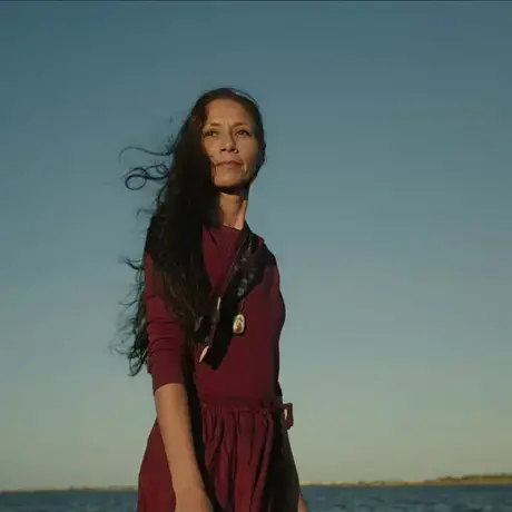 Woman in burgundy dress stands in front of setting sun